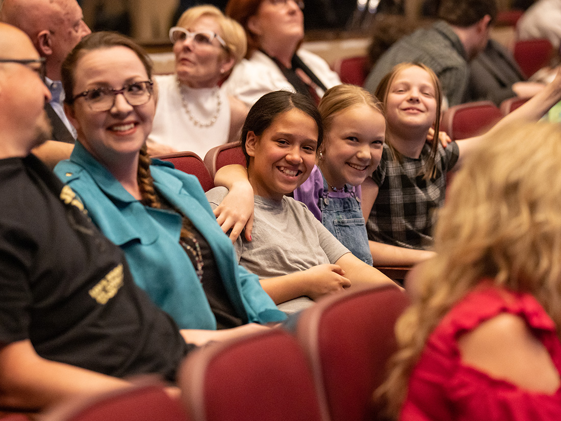 Three young girls sit in the Vantrease PACE Auditorium and smille at the camera.